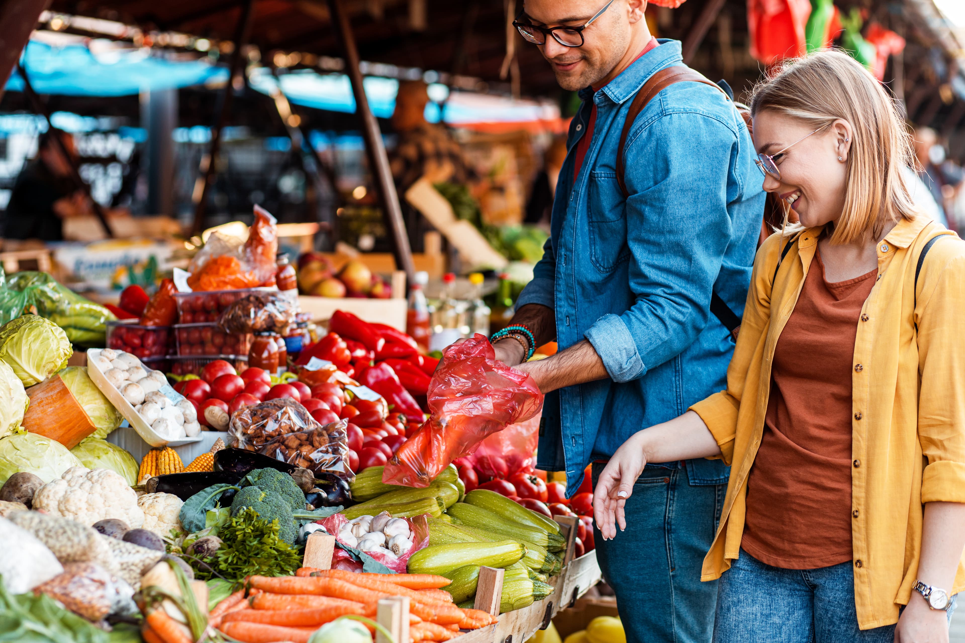 A couple shops for vegetables at a market stand.