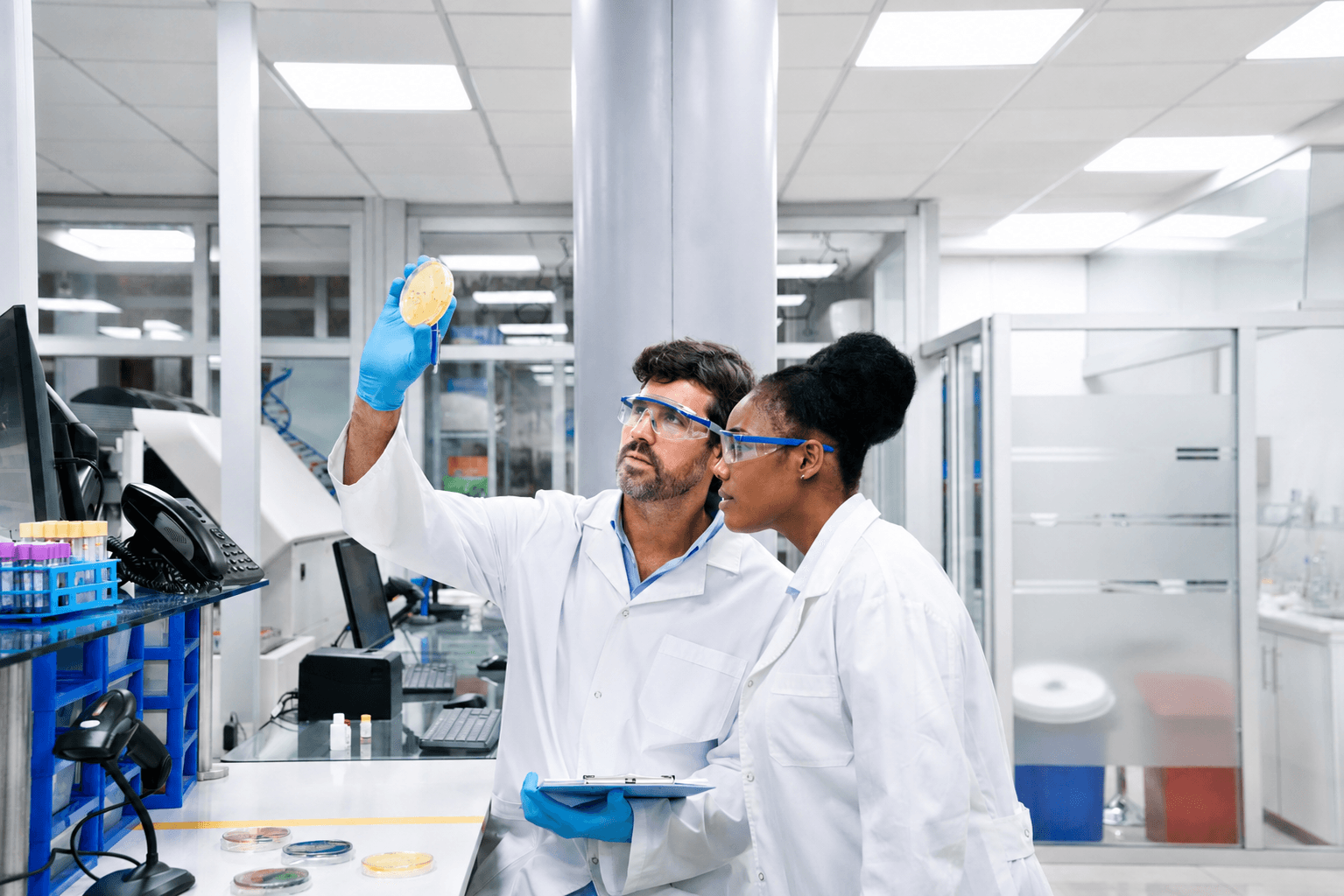 Two laboratorians looking at a petri dish held up to the light.