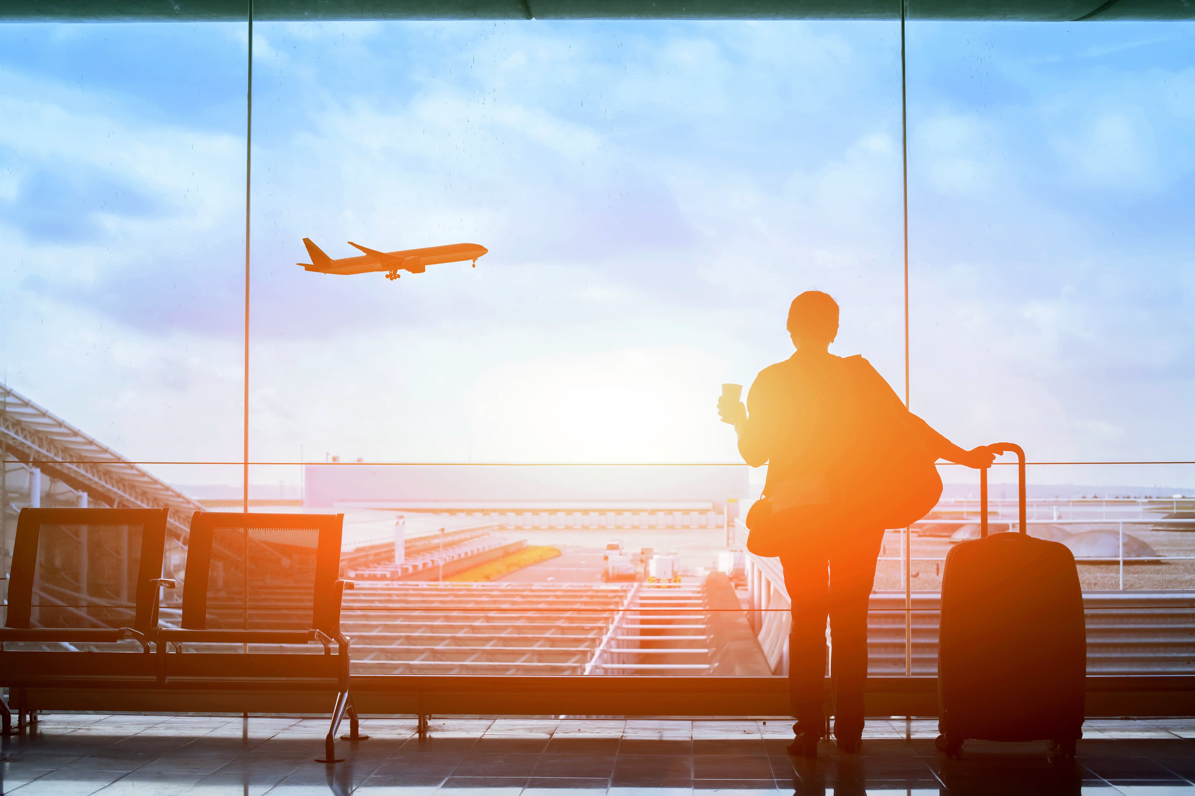 A traveler in an airport terminal watches a plane take off.